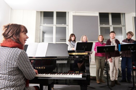 Annemarie Willems achter de piano tijdens lesgeven van koor